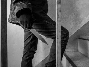 A black and white image on a man climbing some stairs holding a knife.